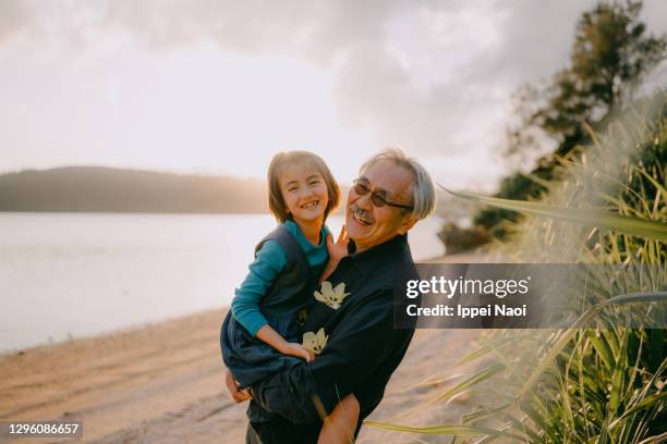 grandfather cuddling granddaughter on beach at sunset, japan - granddaughter stock pictures, royalty-free photos & images