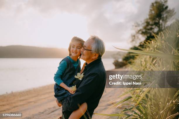 grandfather cuddling granddaughter on beach at sunset - japanese ol stockfoto's en -beelden