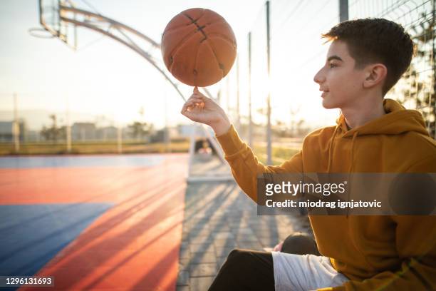 teenage boy spinning basketball ball on sports court - boys basketball stock pictures, royalty-free photos & images