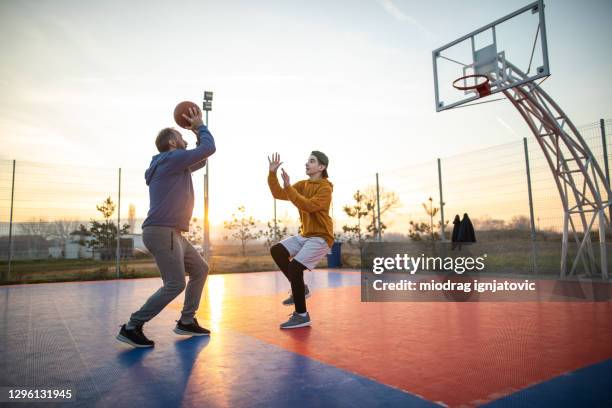 vader en zoon die basketbal op openluchthof spelen - shooting baskets stockfoto's en -beelden