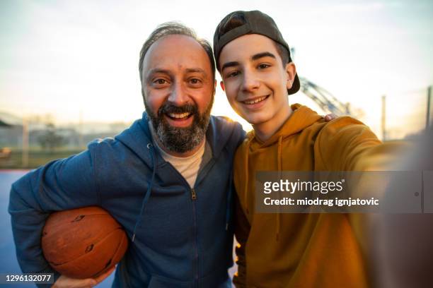 padre e figlio si fanno selfie sul campo da basket all'aperto - figlio maschio foto e immagini stock