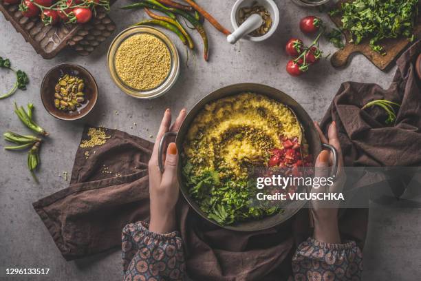 woman hands holding bowl with millet, tomatoes and greens on dark concrete background. food composition with ingredients and towel. - millet stock pictures, royalty-free photos & images