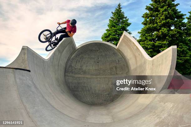 male rider with bmx bike jumping on concrete ramp against sky at skateboard park - rampe stock-fotos und bilder