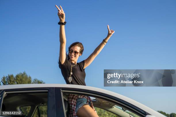 young female standing in car through sunroof making a peace sign - sunroof stock pictures, royalty-free photos & images