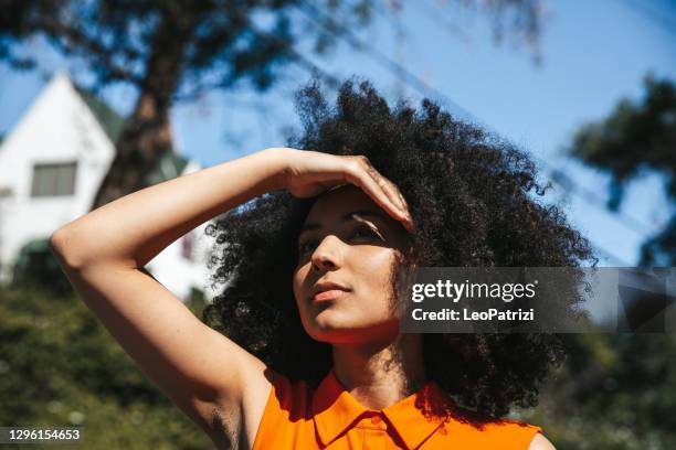 frau mit afro-haar bedeckt ihre augen von der sonne - sun on face stock-fotos und bilder