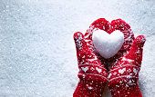 Female hands in knitted mittens with snowy heart against snow background