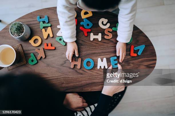overhead view of mother teaching little daughter alphabets. they create words and spells out the word "home" with colourful wooden capital letters while playing and homeschooling at home. family lifestyle and homeschooling theme - hometown stock-fotos und bilder