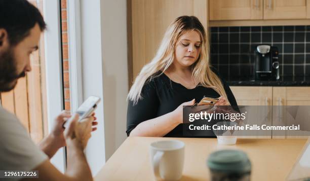 a couple ignore each other at the kitchen table, while they both stare down at their mobile phones - friendship breakup stock pictures, royalty-free photos & images