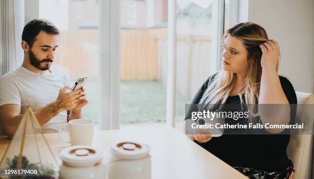 a woman looks insecure as her partner ignores her to look at his phone - ignorance foto e immagini stock