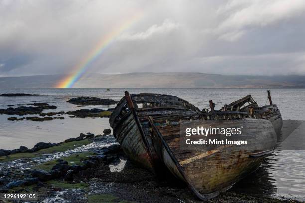 rainbow and beached old wooden fishing boats on shore at salen - shipwreck stock pictures, royalty-free photos & images