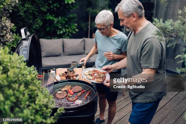senior-paar genießen im hinterhof und grillfleisch - männer grillen stock-fotos und bilder