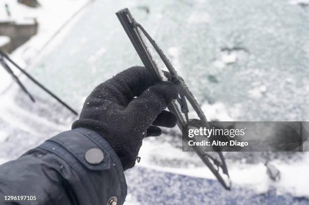 a person holds an icy car wiper while cleaning it on a snowy day in winter. germany. - ruitenwisser stockfoto's en -beelden