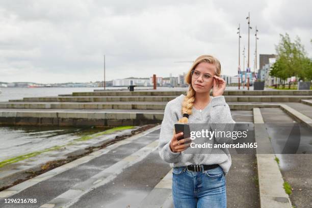 serious woman with tight braid browsing smartphone and looking away - andersdahl65 stock pictures, royalty-free photos & images