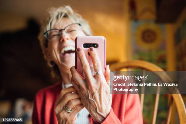 senior woman laughing while using her smartphone - alleen seniore vrouwen stockfoto's en -beelden