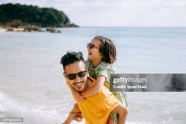 father giving piggyback ride to young daughter on beach, japan - parent and child stock pictures, royalty-free photos & images