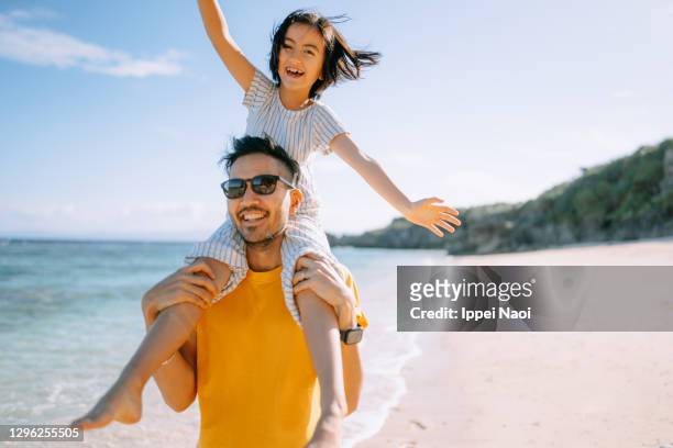 father carrying young daughter on shoulders on beach - beach holiday stock pictures, royalty-free photos & images