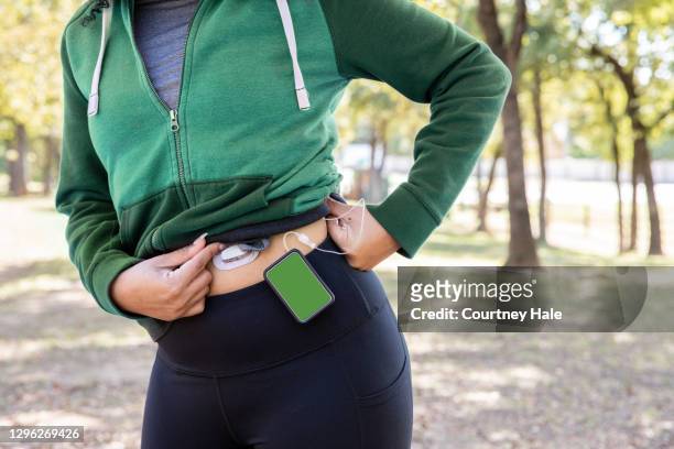 連続的なインスリンポンプと空白の緑色のスクリーンを持つ血糖値モニターを身に着けている認識できない女性は、自然の中で屋外ハイキングです - 油井やぐら ストックフォトと画像