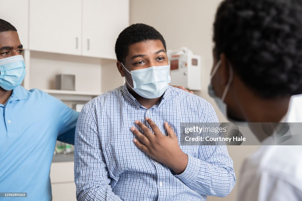 Teenage boy explains symptoms to his doctor during the Covid-19 pandemic