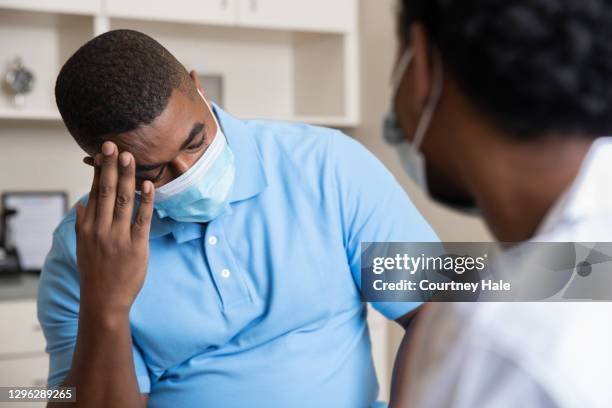 mature man explains head pain to doctor while wearing a protective face mask - bedside manner stock pictures, royalty-free photos & images