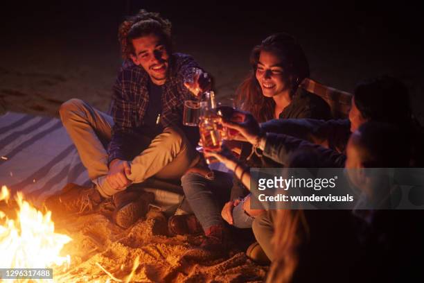 gruppo di amici che brindano a bevande sul falò della spiaggia di notte - bon fire foto e immagini stock