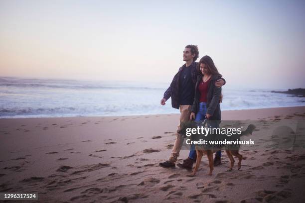 freund und freundin zu fuß hund an der leine am strand - romantic couple walking winter beach stock-fotos und bilder