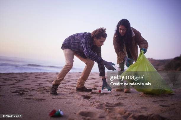 deux amis ramassant des ordures sur la plage pendant le coucher du soleil - volunteer beach photos et images de collection