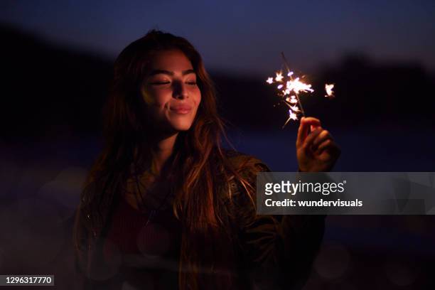 junge schöne mädchen hält funkelnd am strand in der nacht - sparkler firework stock-fotos und bilder