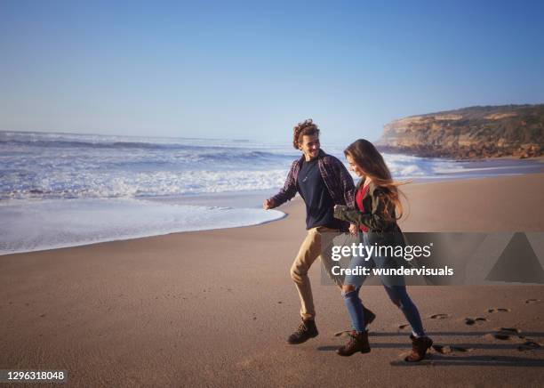 young couple running at the beach during sunset - romantic couple walking winter beach stock pictures, royalty-free photos & images