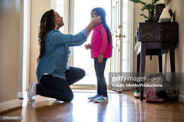 mother putting mask on daughter - woman kneeling stockfoto's en -beelden