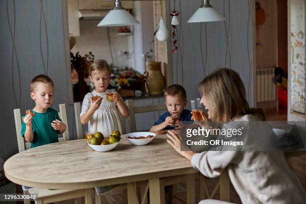 mother with triplets having food and drink at wooden table at home - triplet stock pictures, royalty-free photos & images