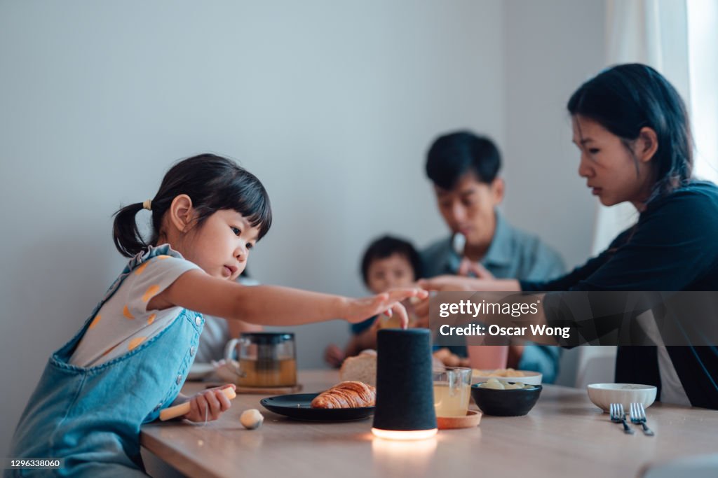 Curious Young Girl Using Smart Speaker While Having Breakfast With Her Family