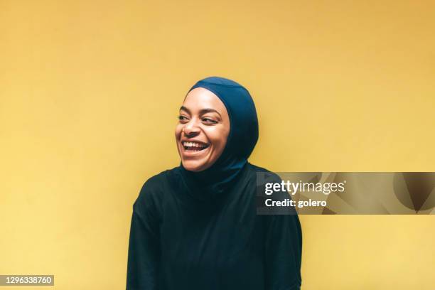 portrait of young laughing muslim sports woman with hijab in front of yellow wall - bright portrait stock pictures, royalty-free photos & images