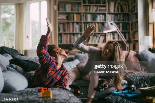 smiling son and mother giving high-five while playing video game on sofa in living room - massively multiplayer online game stock pictures, royalty-free photos & images