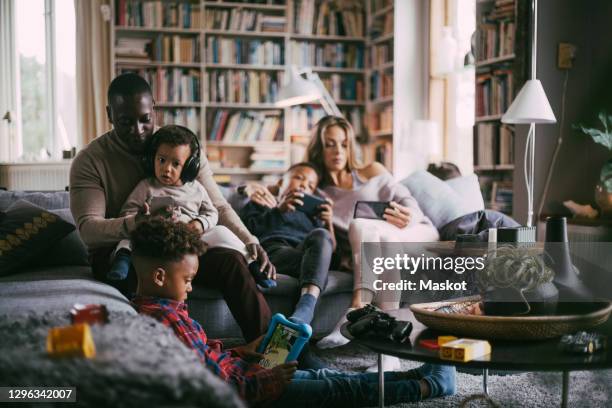 parents and sons using mobile phone while sitting on sofa in living room - wifi stockfoto's en -beelden