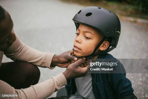 father adjusting son's helmet on footpath - casco herramientas profesionales fotografías e imágenes de stock