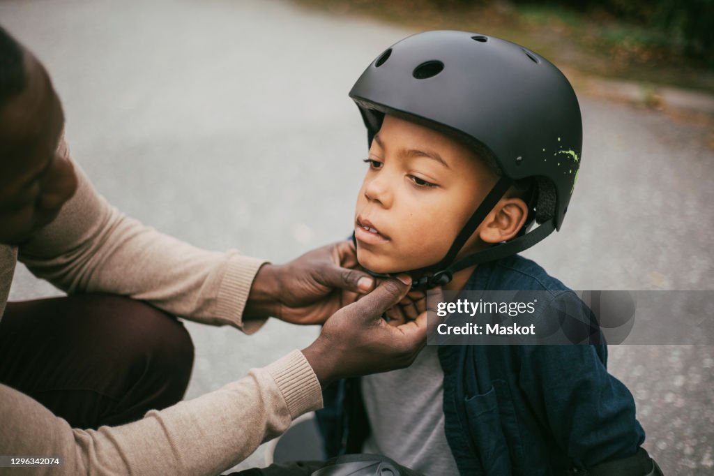 Father adjusting son's helmet on footpath