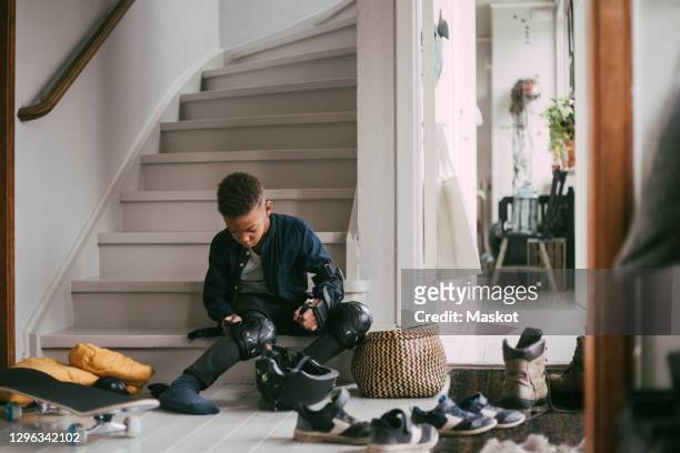 boy wearing kneepad while sitting on staircase at home - sports hall stock pictures, royalty-free photos & images