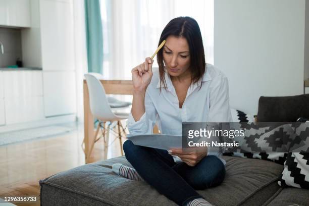 mujer preocupada leyendo documento sentado en casa - arrendatario fotografías e imágenes de stock