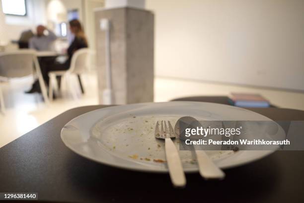 selected focus, empty and dirty white dish with stainless spoon and fork, and on black table after finish meal, and background of blur kitchen, office's canteen and people eat together. - restaurant düsseldorf bildbanksfoton och bilder