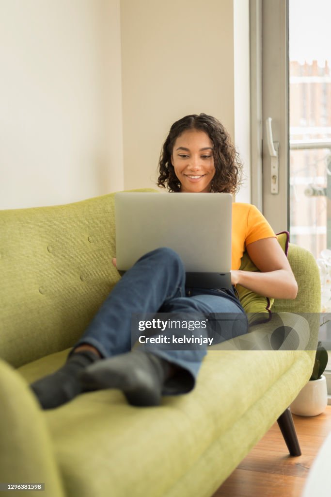 Happy young woman at home on sofa using a laptop