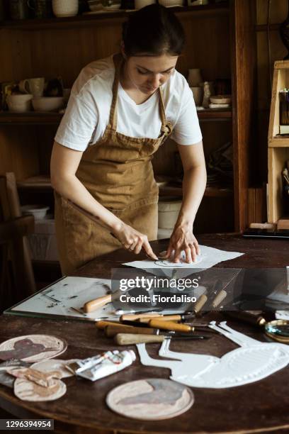 portrait of a woman in an apron holding working tools. roller for applying black ink to a stamp for printing an engraving - linocut stock pictures, royalty-free photos & images