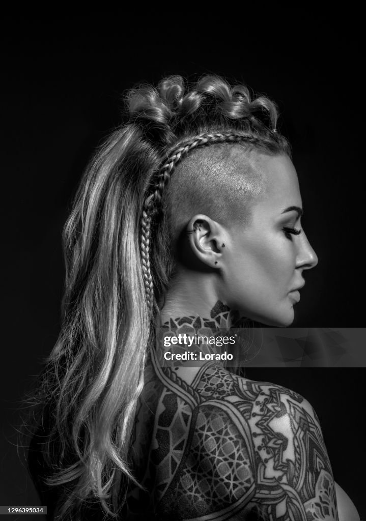 Retrato lateral de uma mulher loira viking tatuada e seu penteado único
