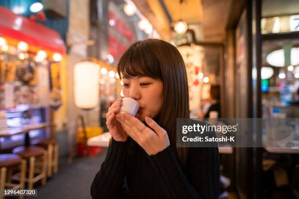 young woman drinking japanese 'saki' rice wine at izakaya bar - sake stock pictures, royalty-free photos & images