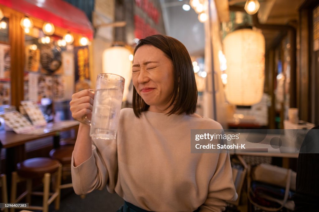 Young woman satisfied with alcohol at Izakaya bar after work