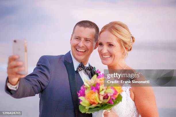 bride and groom take a selfie while on the beach at sunset - sunset beach bouquet wedding couple stock pictures, royalty-free photos & images