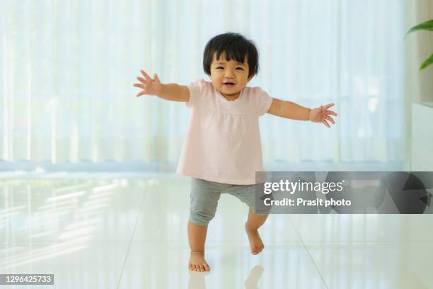 asian toddler baby girl kid toddler in make first steps in living room at home. - baby standing stock pictures, royalty-free photos & images
