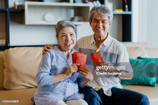 happy senior asian couple holding red envelopes for chinese new year - 70 year male stock pictures, royalty-free photos & images