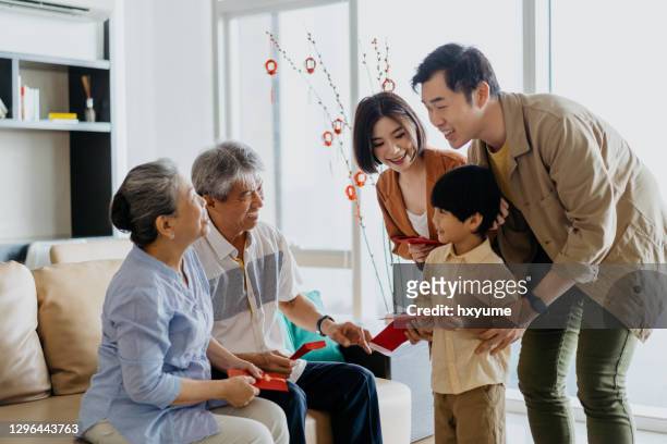 aziatische chinese grootouders die rode envelop aan kleinzoon tijdens chinees nieuwjaar geven - 30 year old men stockfoto's en -beelden