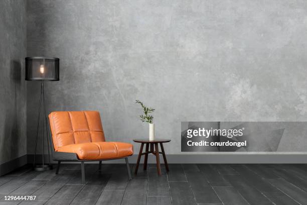 interni moderni con poltrona in pelle color arancio, sconce, tavolino e parete grigia. - sedia foto e immagini stock