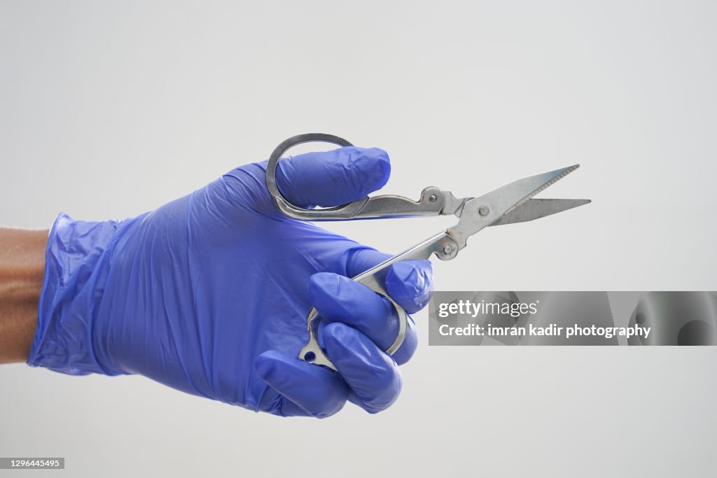 Hand with latex glove holding scissors